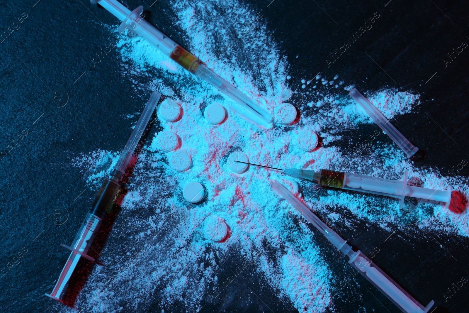 Photo of Drug addiction. Powder, pills and syringes on dark table in neon lights, flat lay