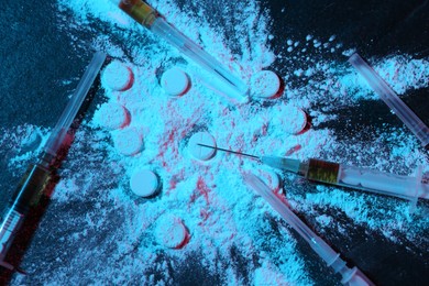 Photo of Drug addiction. Powder, pills and syringes on dark table in neon lights, flat lay