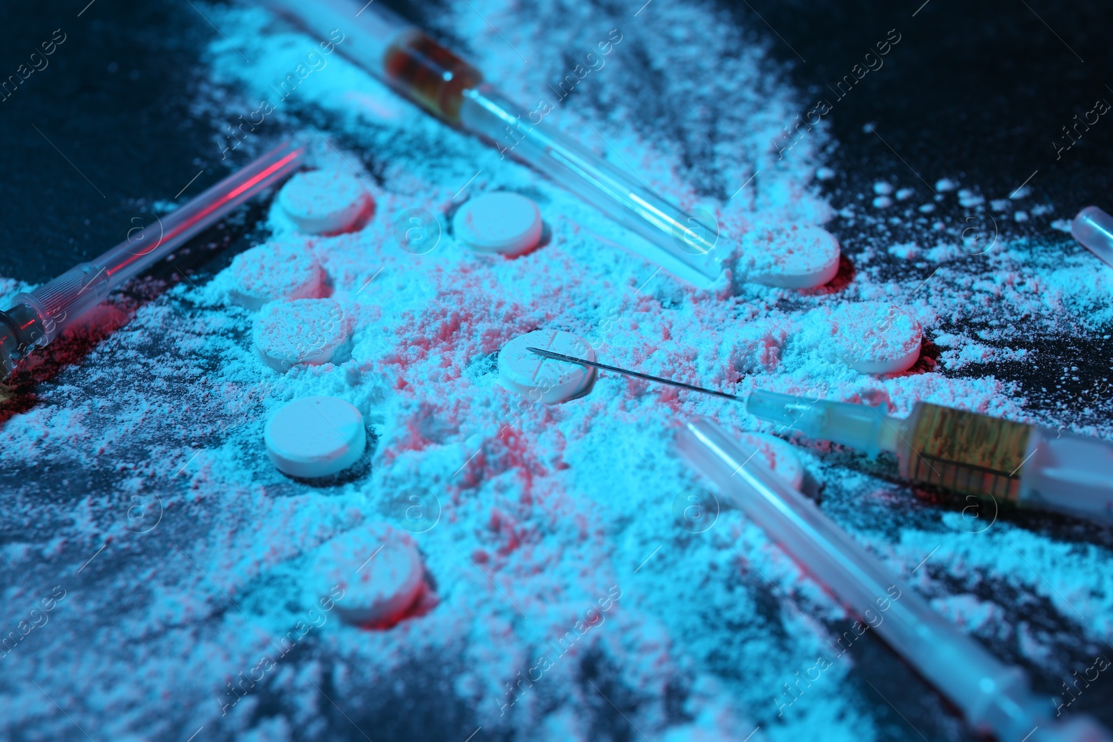 Photo of Drug addiction. Powder, pills and syringes on dark table in neon lights, closeup