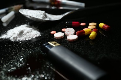 Photo of Drug addiction. Spoon with powder, pills and cigarette lighter on black table, closeup