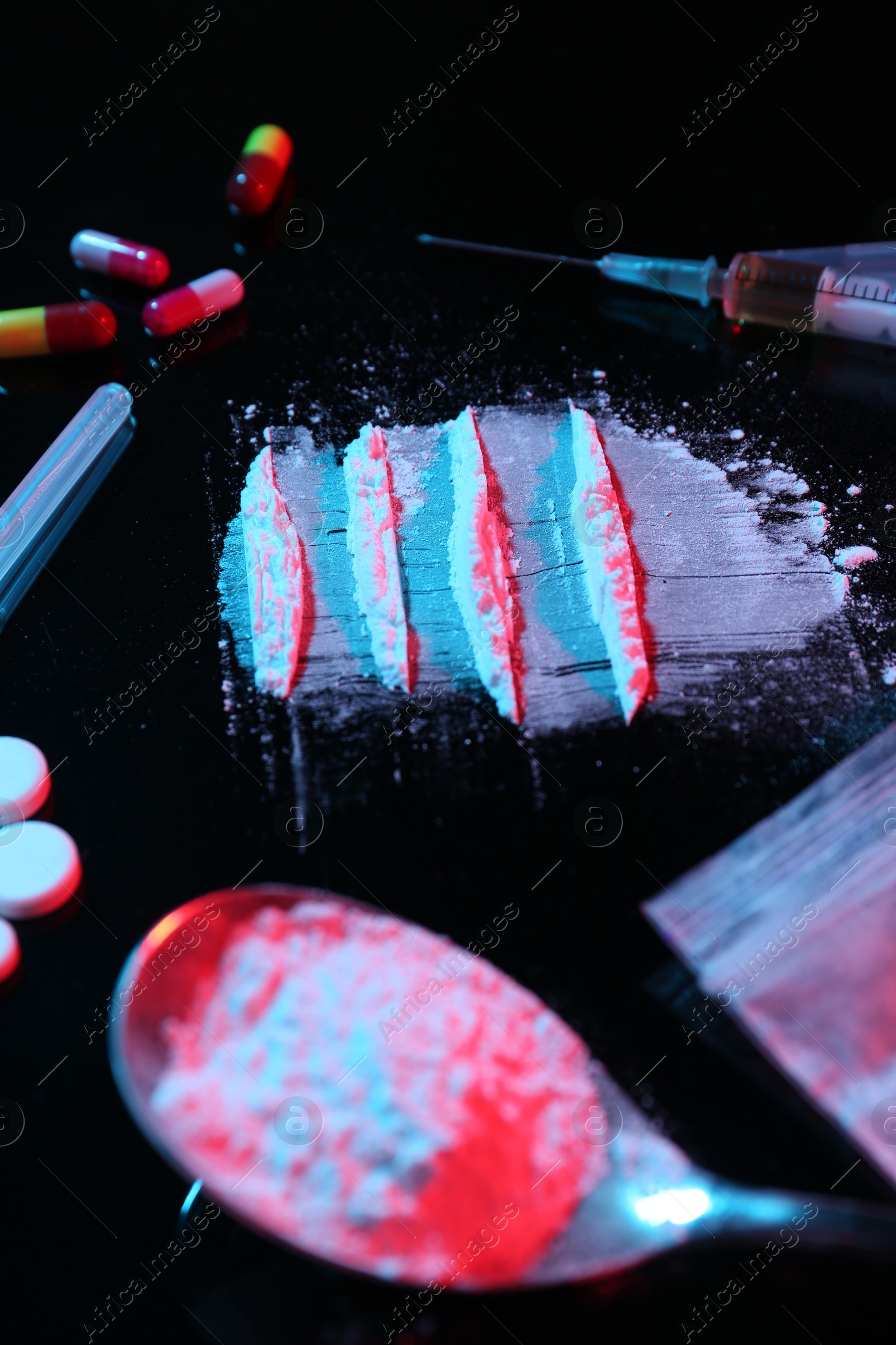 Photo of Drug addiction. Powder, pills, syringe and spoon on black table in neon lights, closeup