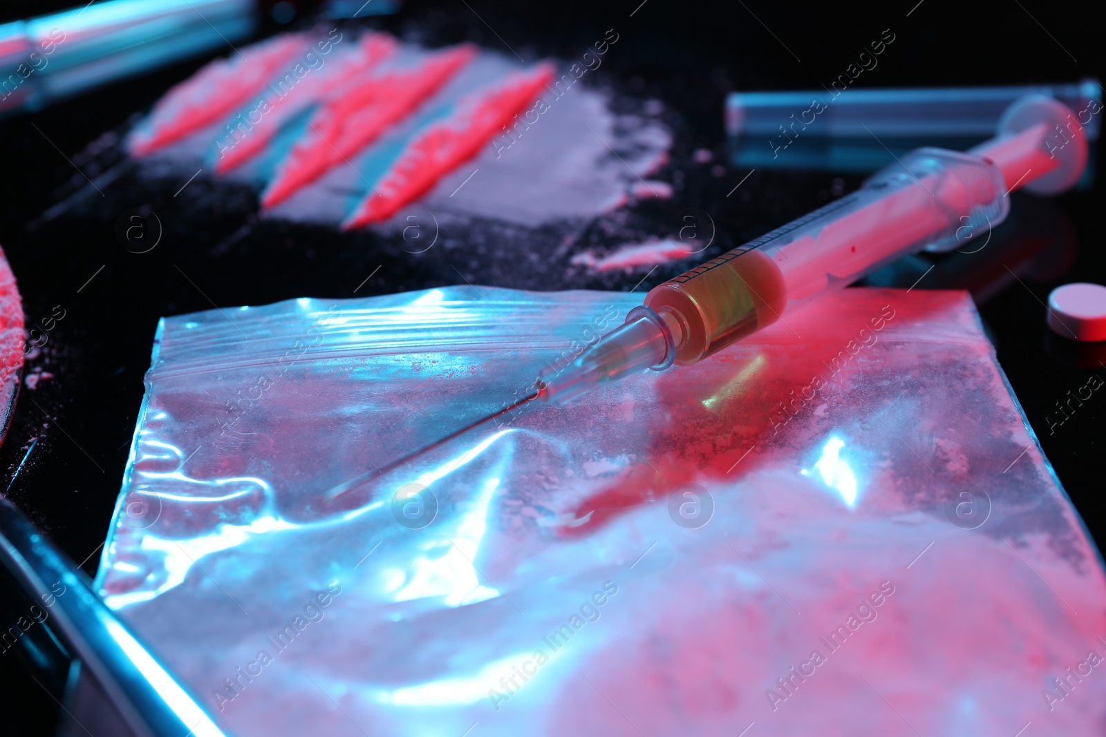 Photo of Drug addiction. Plastic bag with powder and syringe on black table in neon lights, closeup