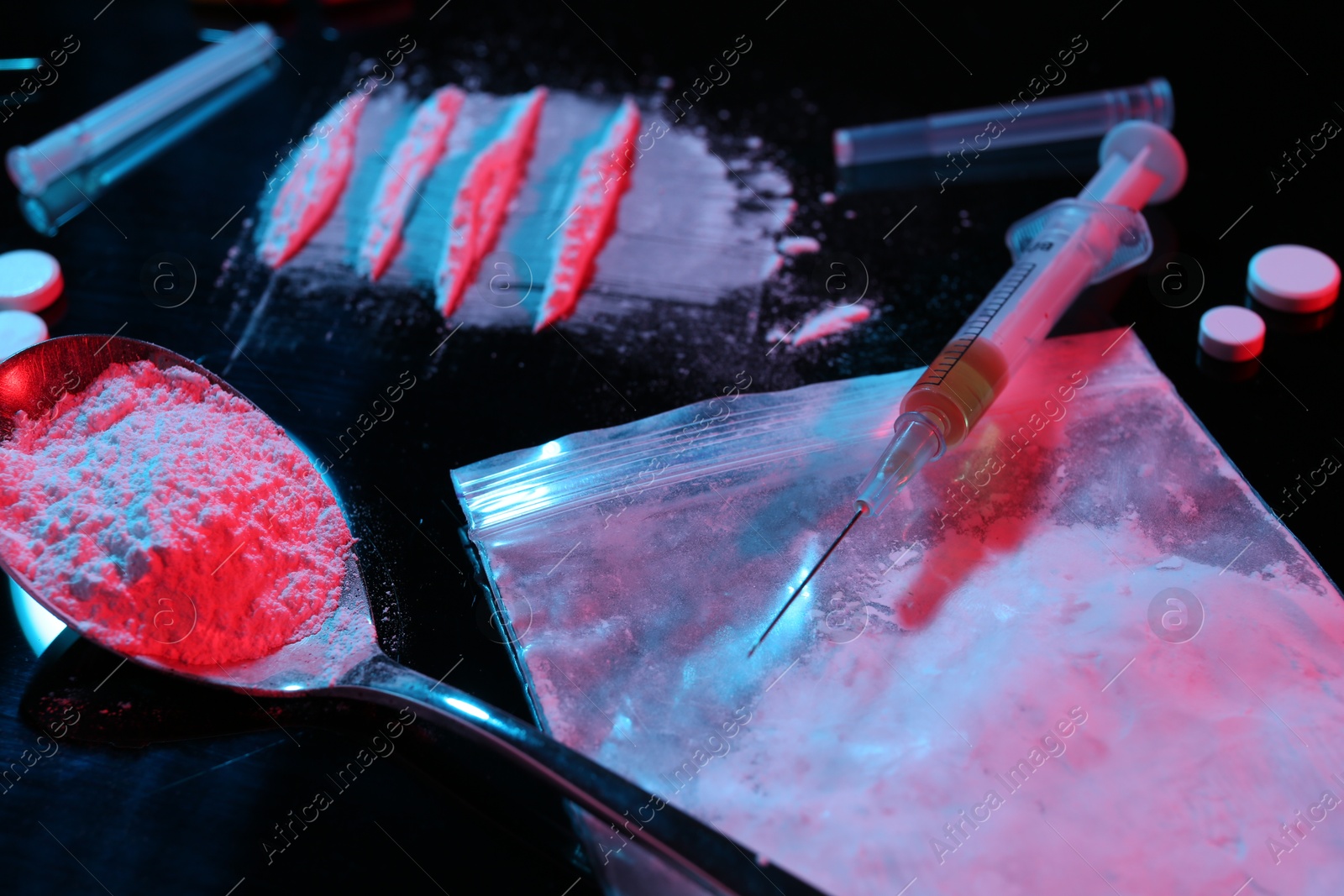 Photo of Drug addiction. Plastic bag with powder, syringe and spoon on black table in neon lights, closeup