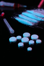 Photo of Drug addiction. Pills and powder on black table in neon lights, closeup