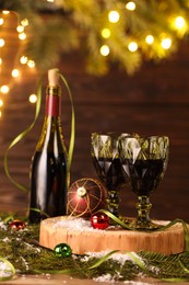 Photo of Red wine and beautiful Christmas decor on wooden table against blurred festive lights