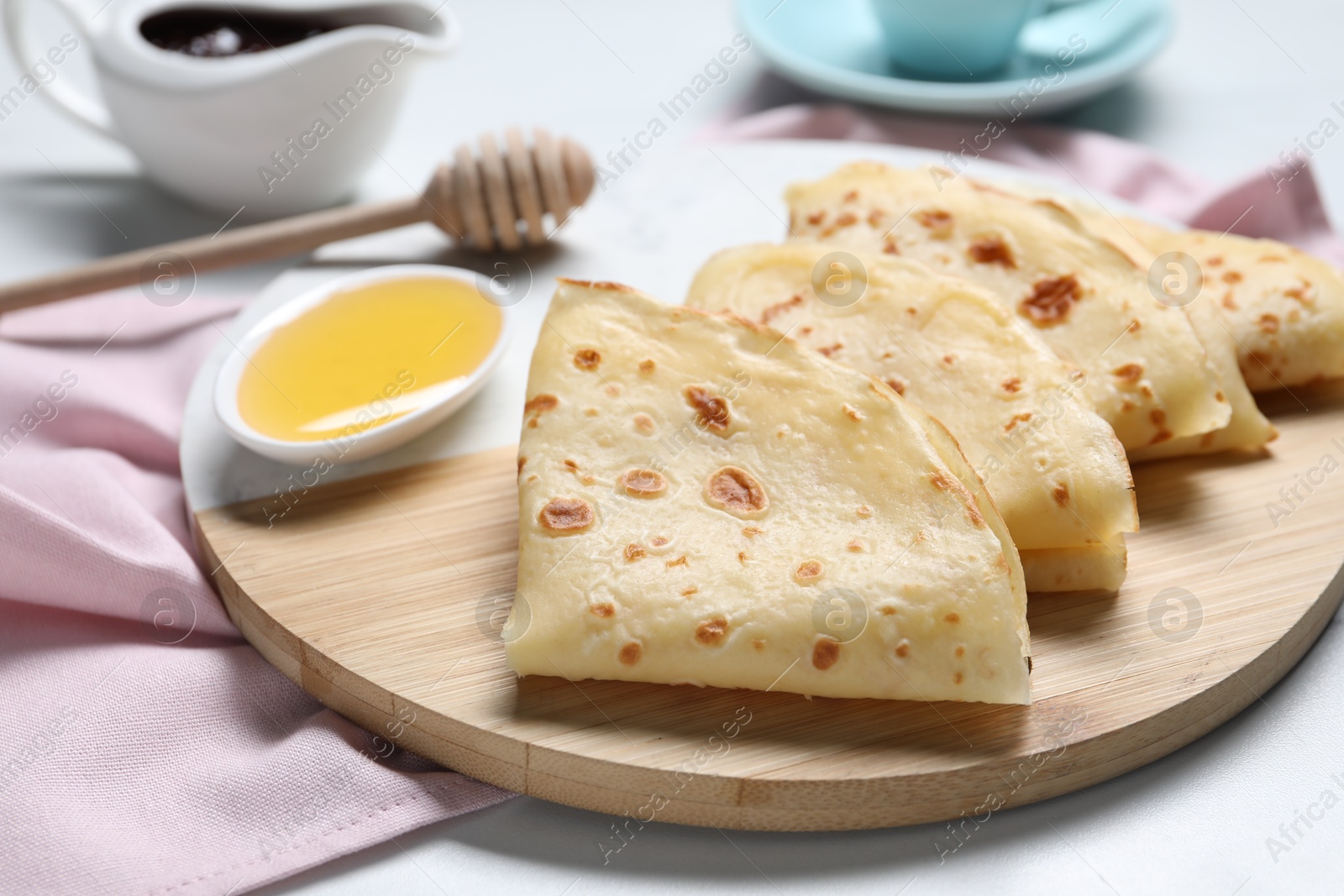 Photo of Delicious crepes and honey on light table, closeup