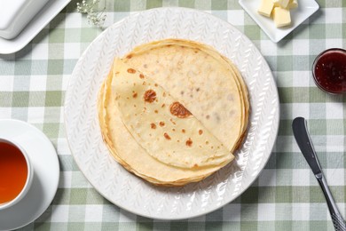 Photo of Delicious crepes, tea, butter and jam on table, flat lay