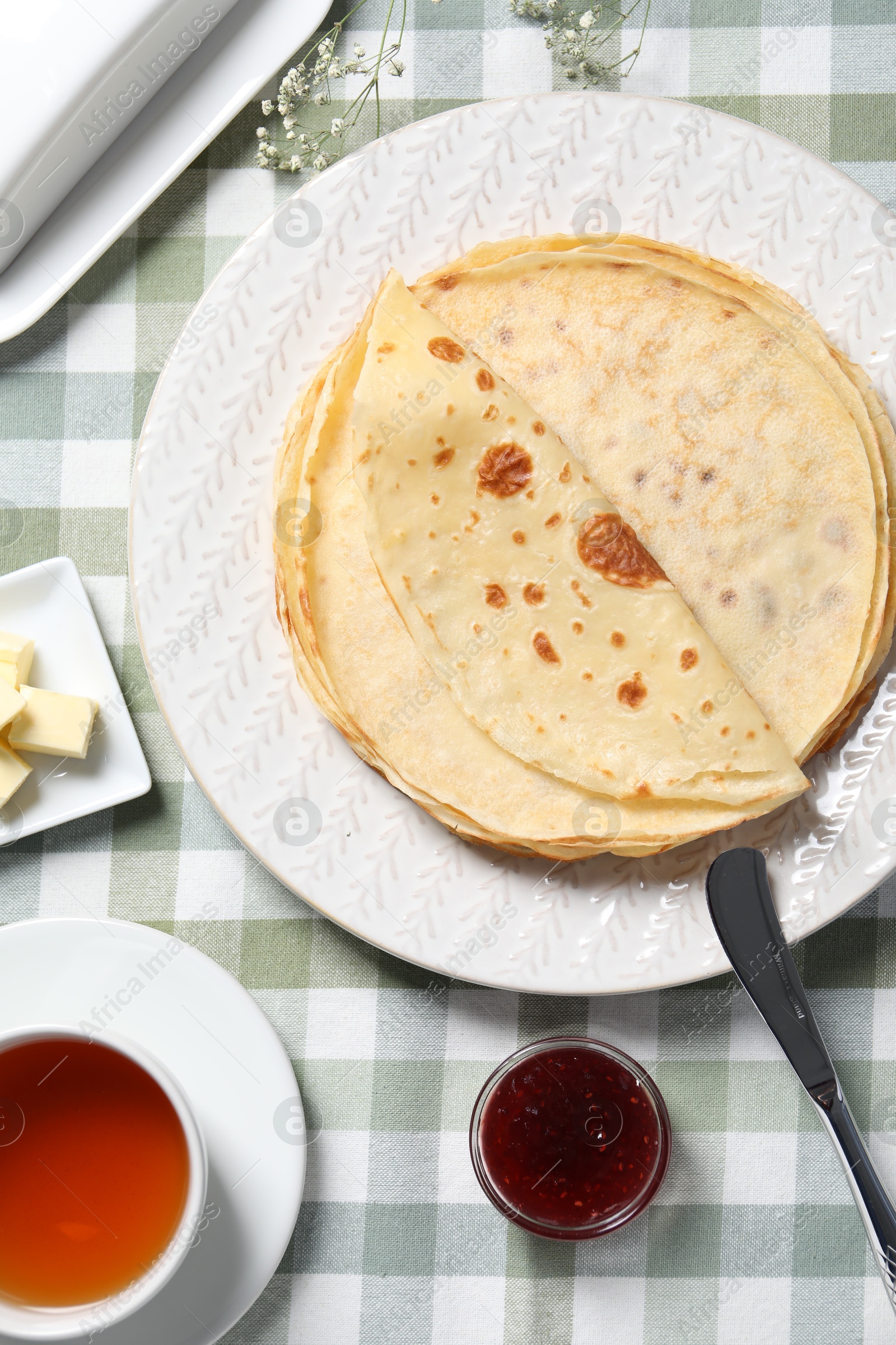 Photo of Delicious crepes, tea, butter and jam on table, flat lay