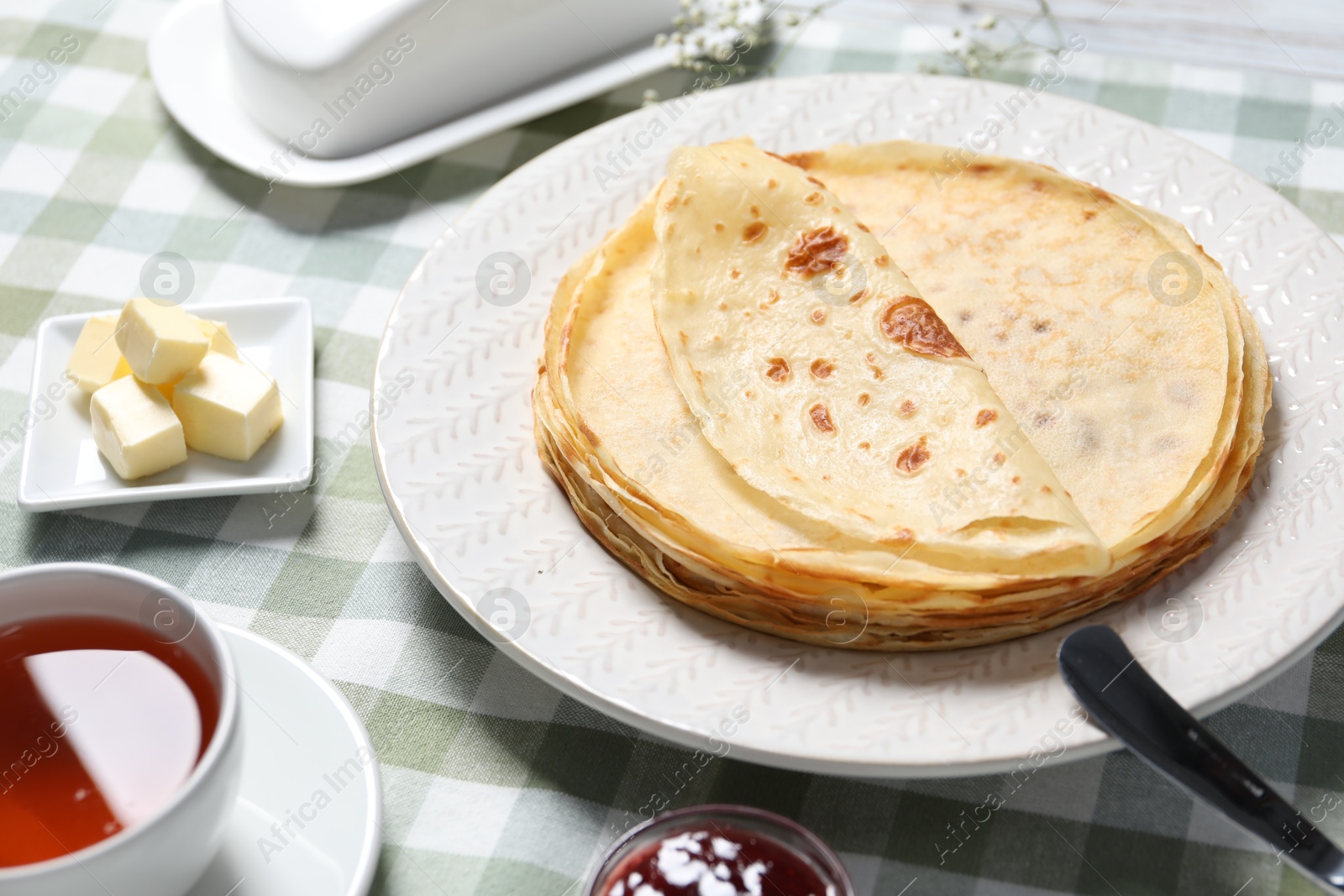 Photo of Delicious crepes, tea and butter on table, closeup view