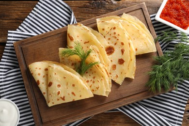 Photo of Delicious crepes, dill, red caviar and sour cream on wooden table, flat lay