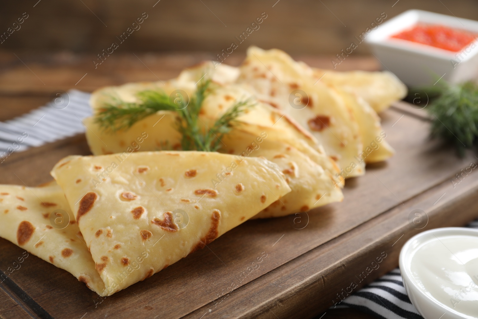 Photo of Delicious crepes, dill and sour cream on table, closeup