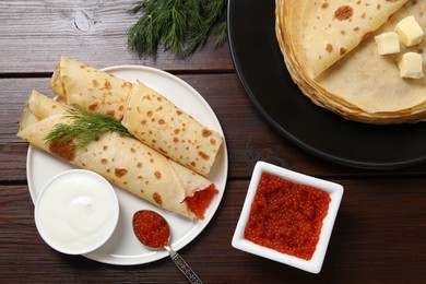 Photo of Delicious crepes with red caviar served on wooden table, flat lay