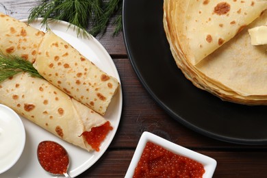 Photo of Delicious crepes with red caviar served on wooden table, flat lay