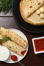 Photo of Delicious crepes with red caviar served on wooden table, flat lay