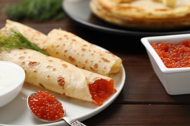 Photo of Delicious crepes with red caviar served on wooden table, closeup