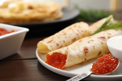 Photo of Delicious crepes with red caviar served on wooden table, closeup