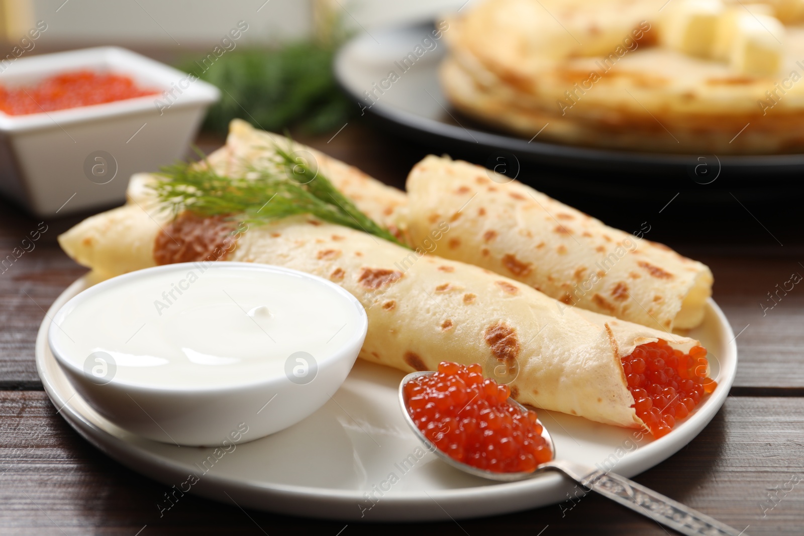 Photo of Delicious crepes with red caviar served on wooden table, closeup