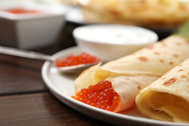 Photo of Delicious crepes with red caviar served on wooden table, closeup