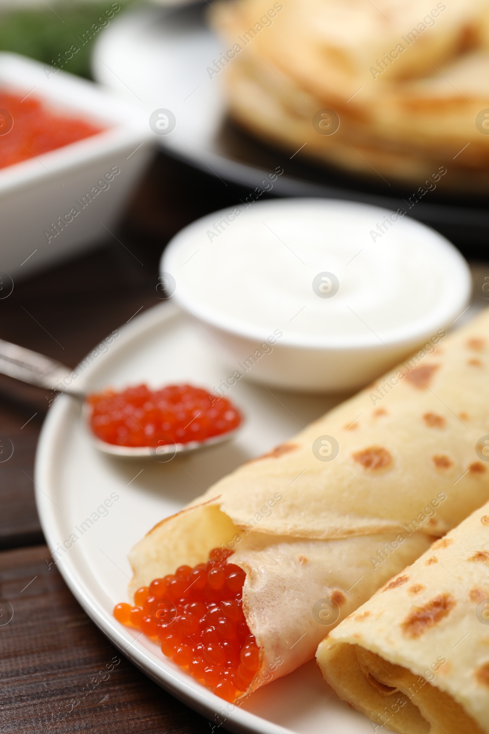 Photo of Delicious crepes with red caviar served on wooden table, closeup