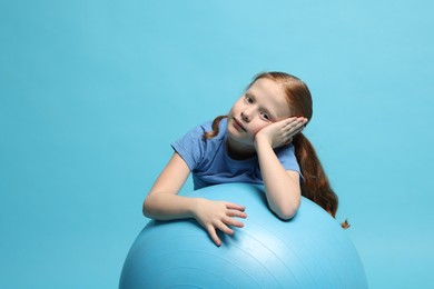 Photo of Cute little girl with fitness ball on light blue background, space for text