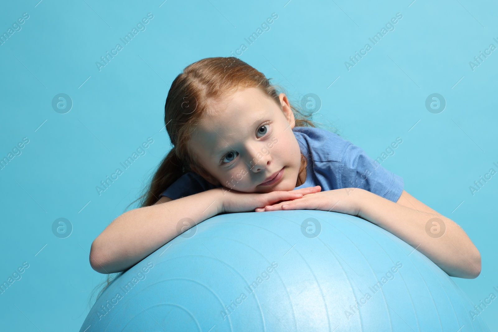 Photo of Cute little girl with fitness ball on light blue background