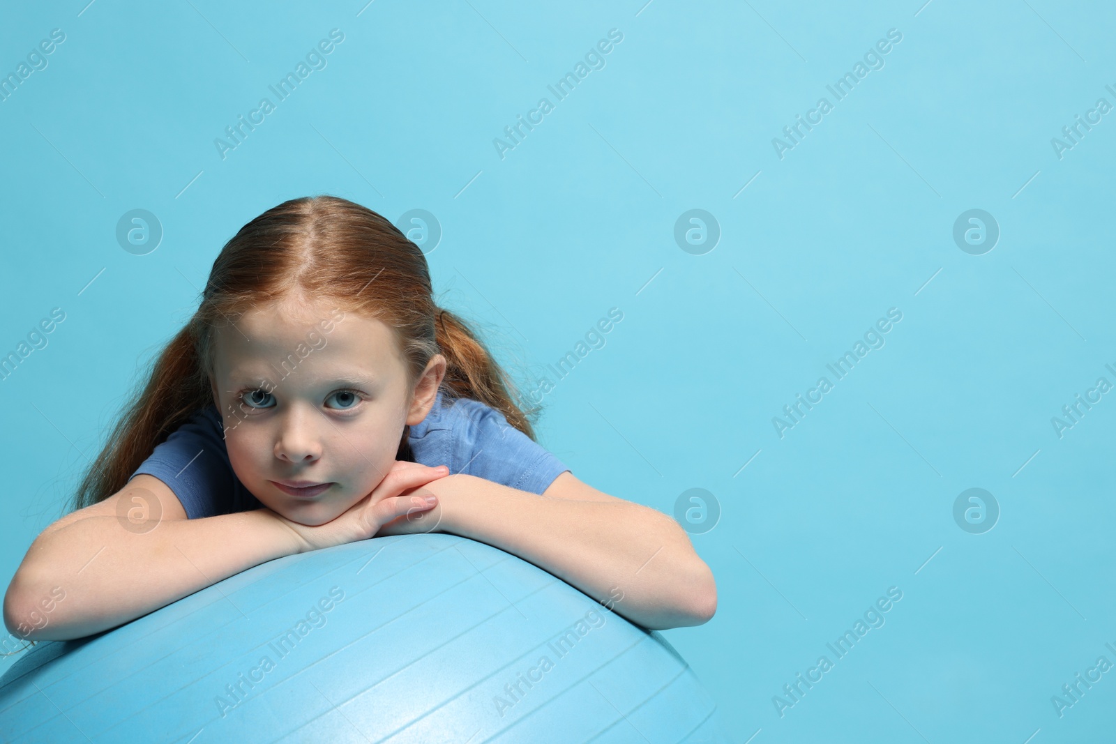 Photo of Cute little girl with fitness ball on light blue background, space for text