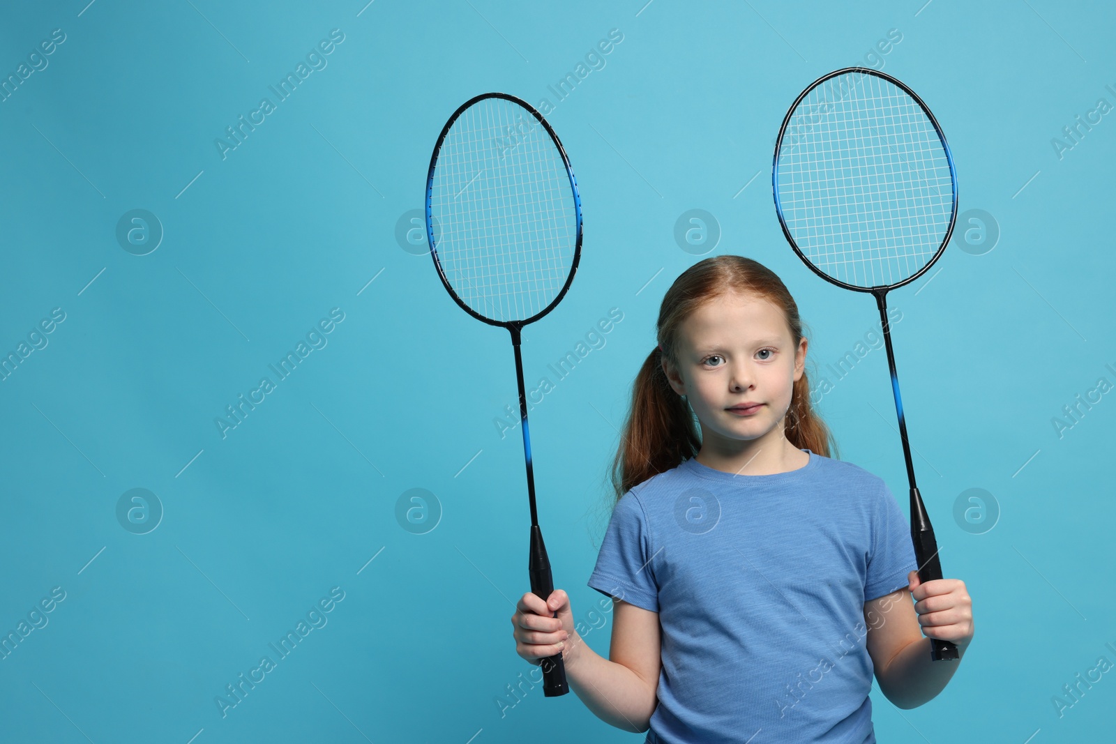 Photo of Little girl with badminton rackets on light blue background, space for text