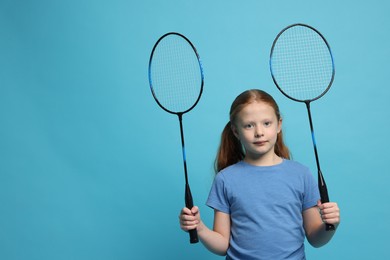 Photo of Little girl with badminton rackets on light blue background, space for text