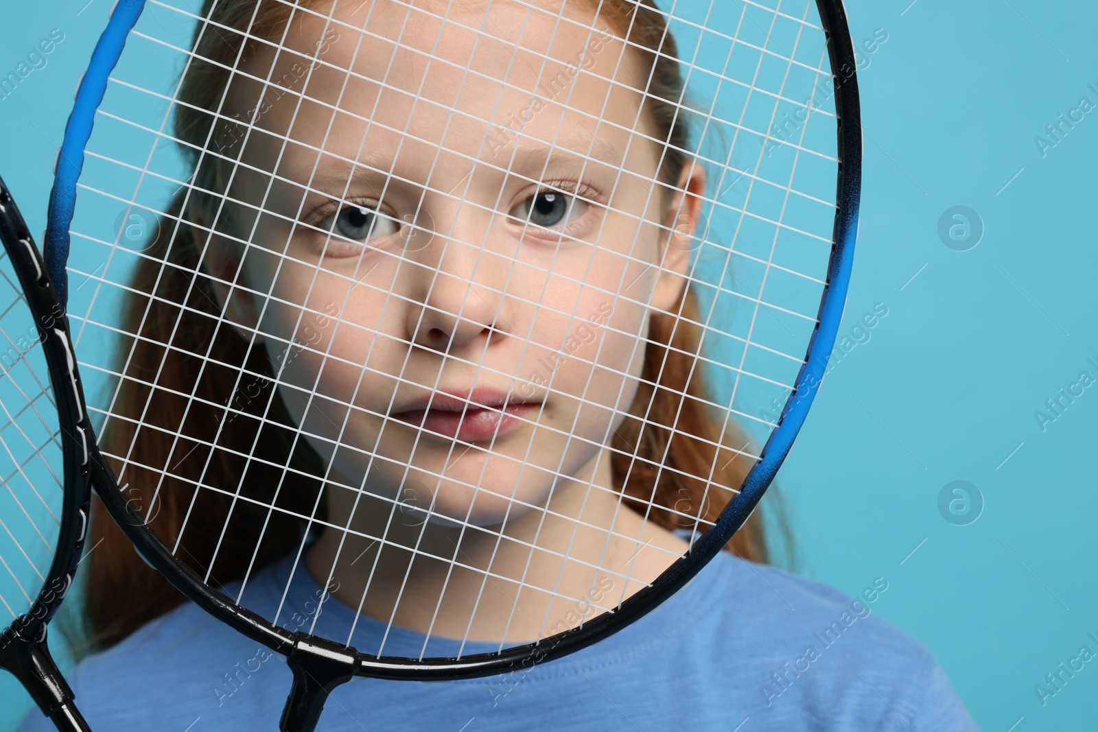 Photo of Little girl with badminton rackets on light blue background