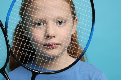 Photo of Little girl with badminton rackets on light blue background