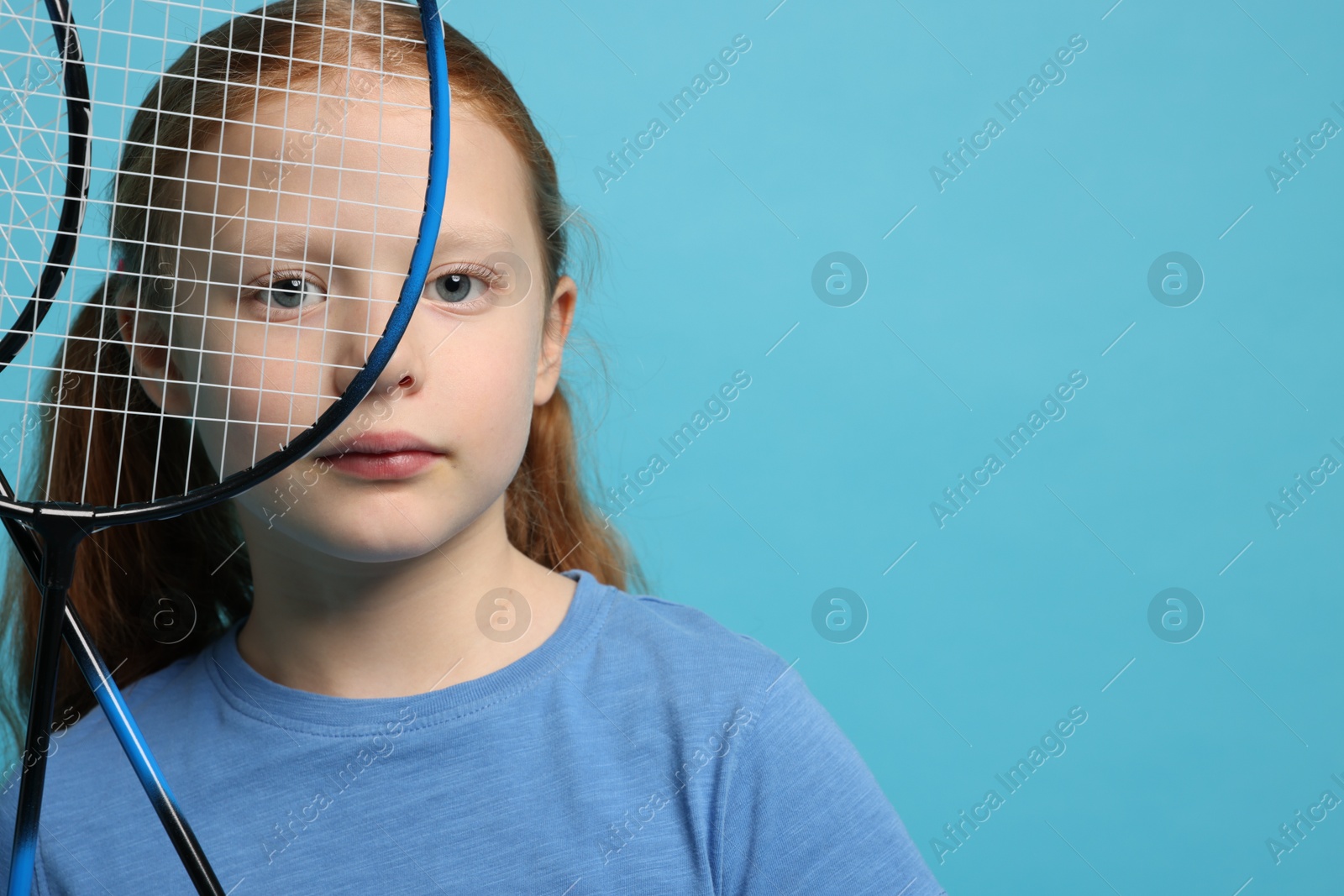 Photo of Little girl with badminton rackets on light blue background, space for text