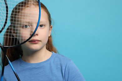 Photo of Little girl with badminton rackets on light blue background, space for text