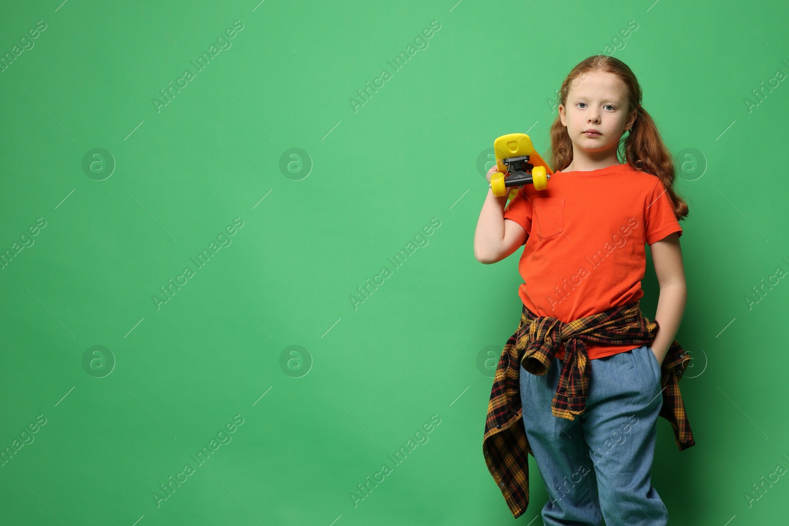 Photo of Stylish little girl with penny board on green background, space for text