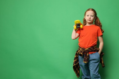 Photo of Stylish little girl with penny board on green background, space for text