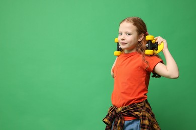 Photo of Stylish little girl with penny board on green background, space for text