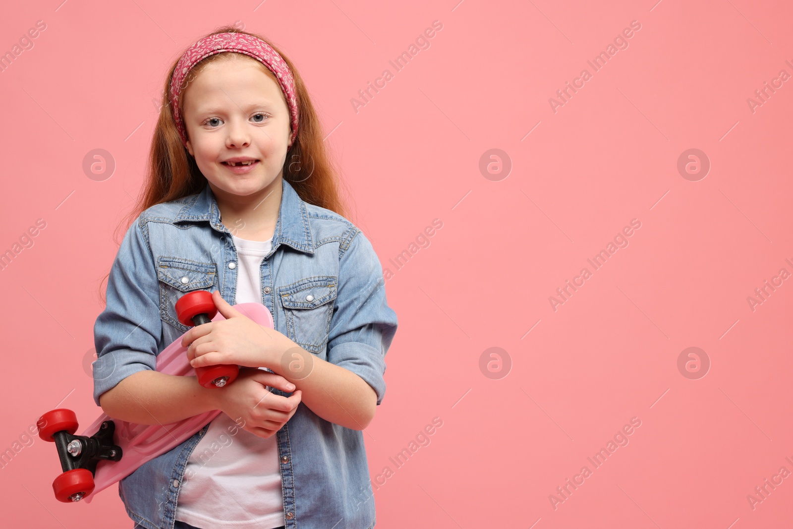 Photo of Little girl with penny board on pink background, space for text