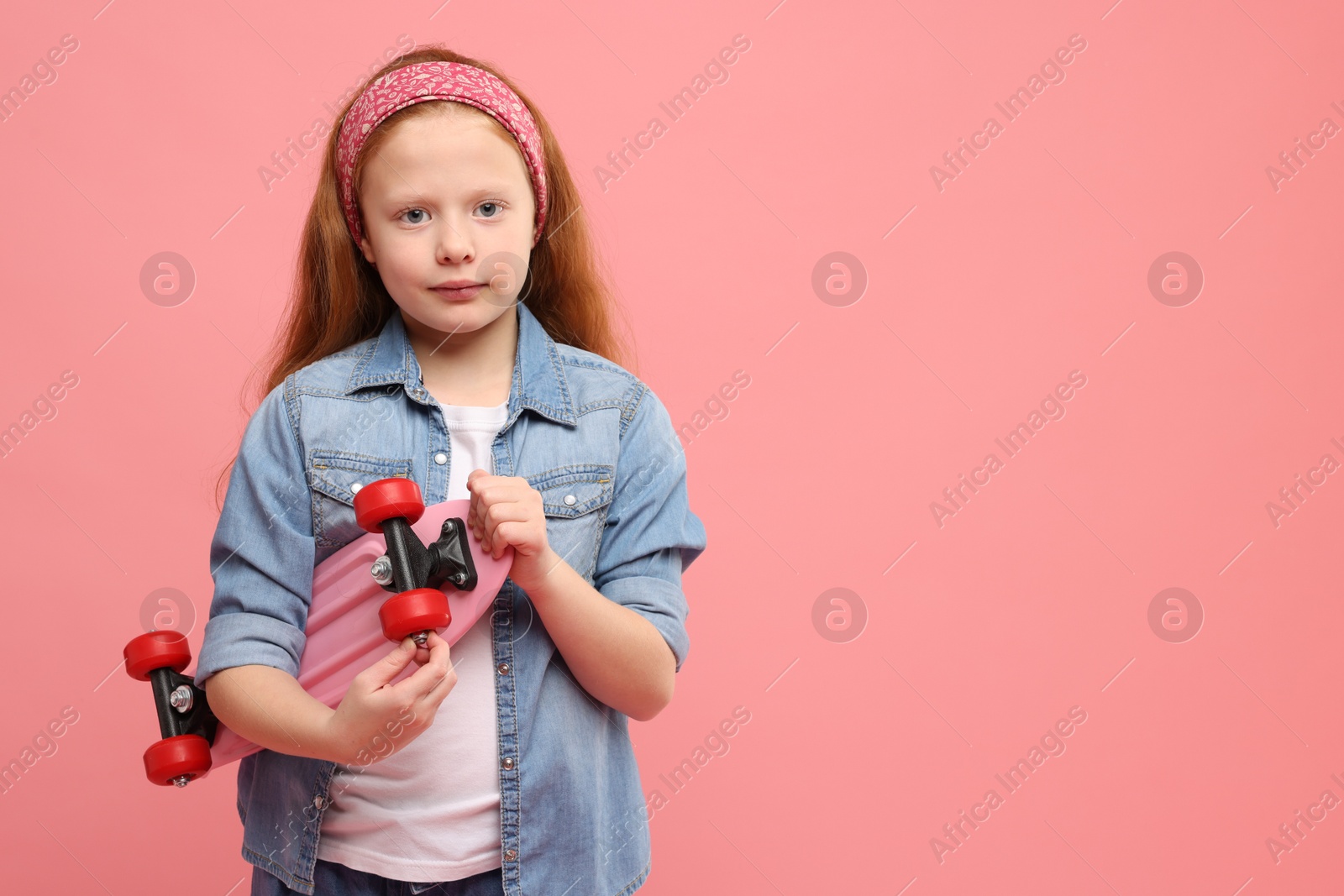 Photo of Little girl with penny board on pink background, space for text