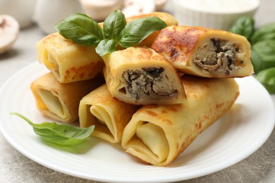 Photo of Delicious rolled crepes with mushrooms and basil on grey table, closeup