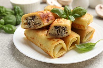 Photo of Delicious rolled crepes with mushrooms and basil on grey table, closeup