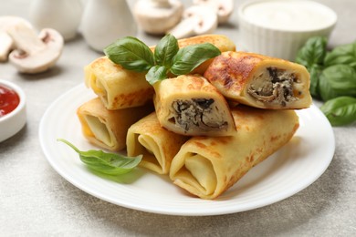 Photo of Delicious rolled crepes with mushrooms and basil on grey table, closeup