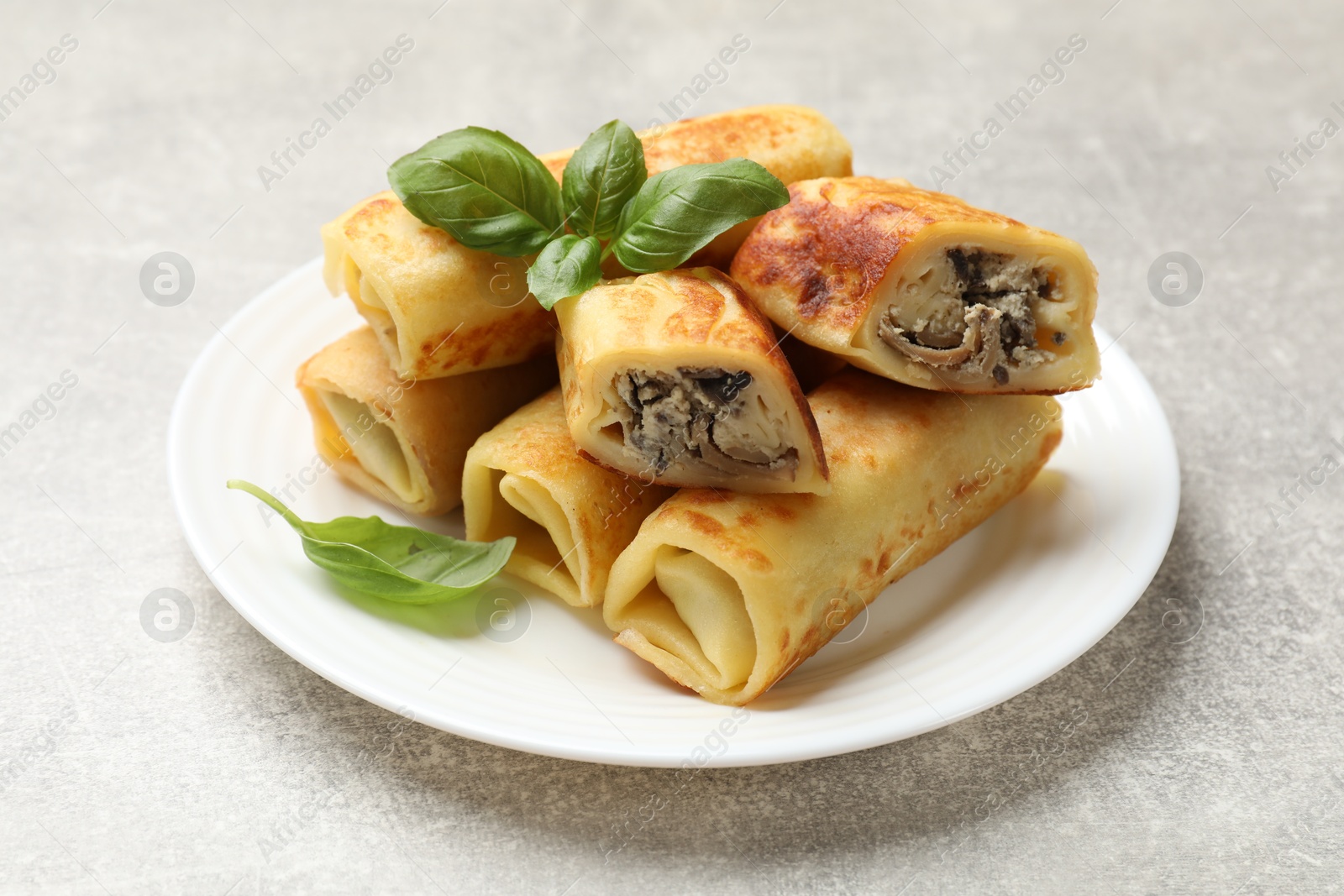 Photo of Delicious rolled crepes with mushrooms and basil on grey table, closeup