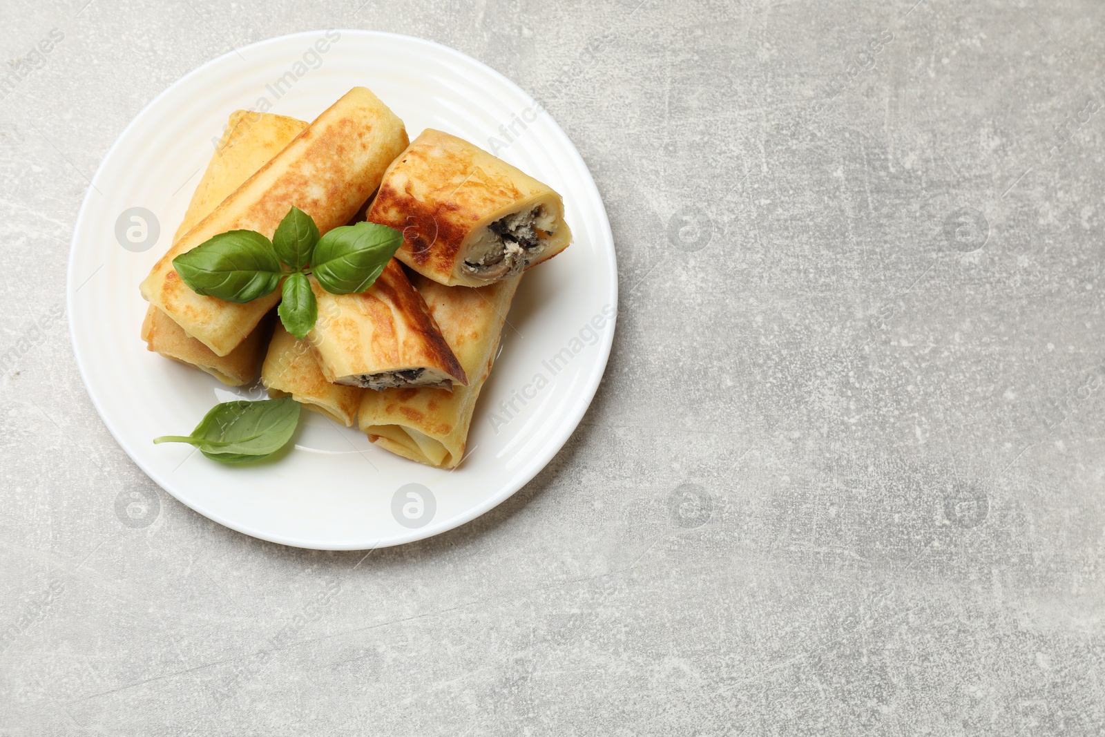 Photo of Delicious rolled crepes with mushrooms and basil on grey table, top view. Space for text