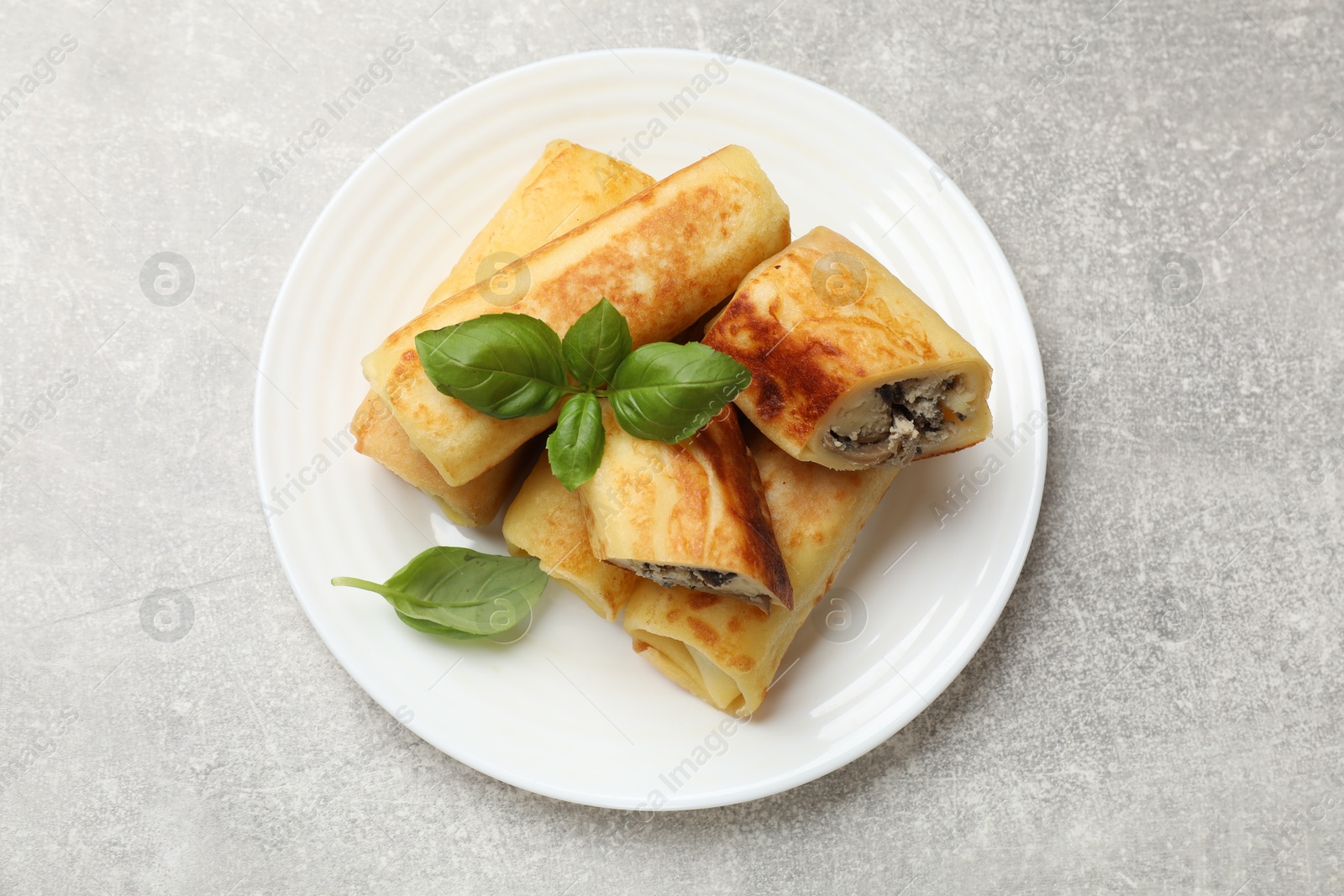 Photo of Delicious rolled crepes with mushrooms and basil on grey table, top view