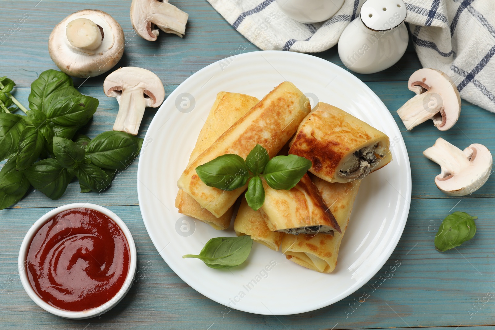 Photo of Delicious rolled crepes with mushrooms, basil and sauce on light blue wooden table, flat lay