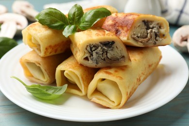 Photo of Delicious rolled crepes with mushrooms and basil on light blue wooden table, closeup