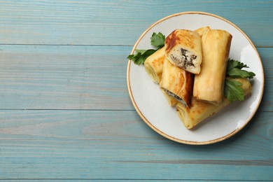 Photo of Delicious rolled crepes with mushrooms and parsley on light blue wooden table, top view. Space for text