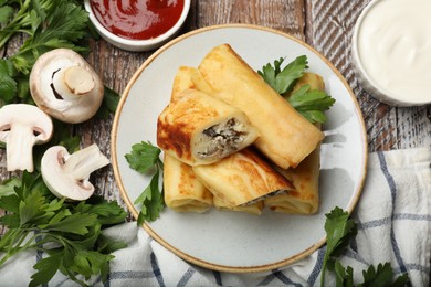 Photo of Delicious rolled crepes with mushrooms, parsley, sour cream and sauce on wooden table, flat lay