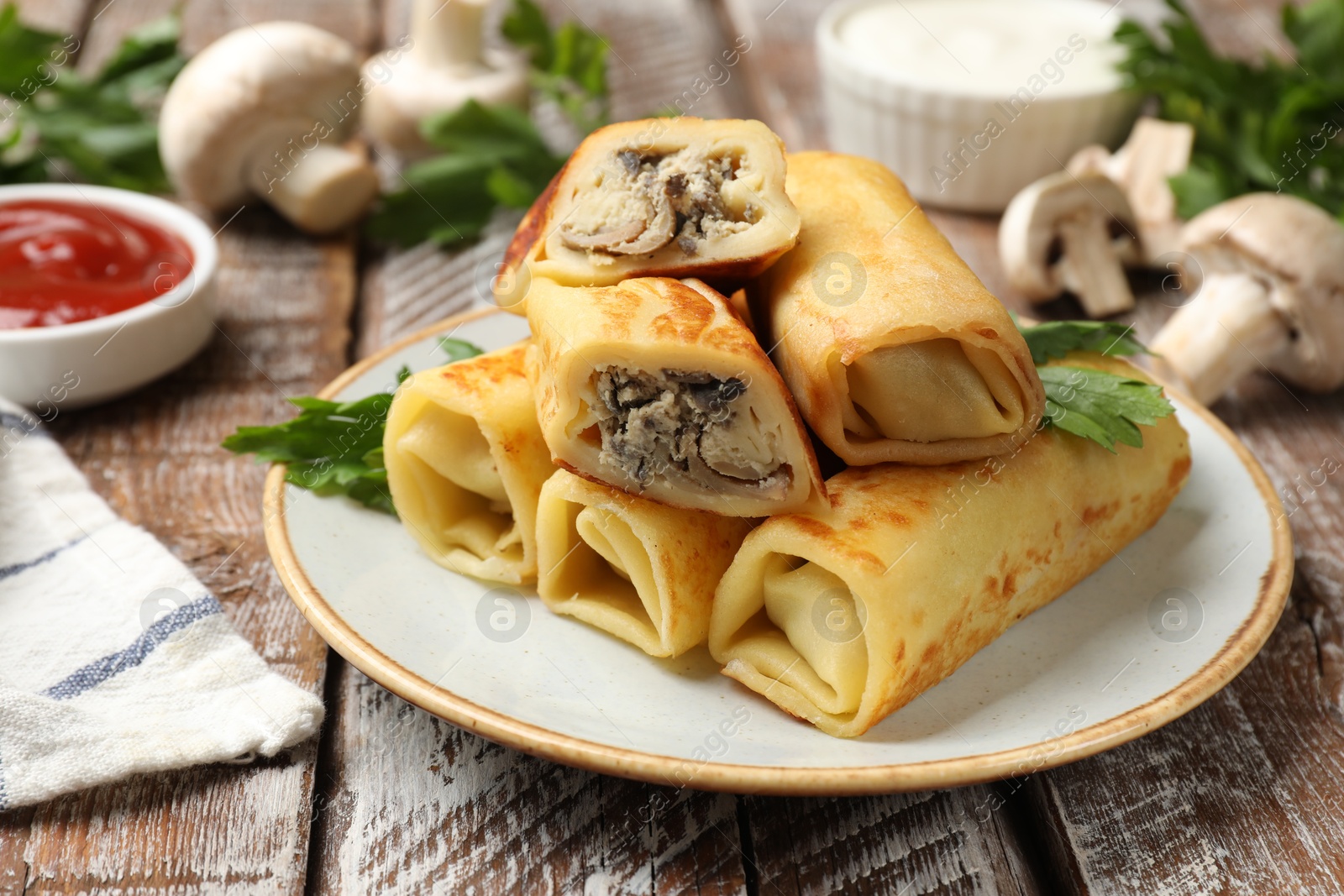 Photo of Delicious rolled crepes with mushrooms and parsley on wooden table, closeup