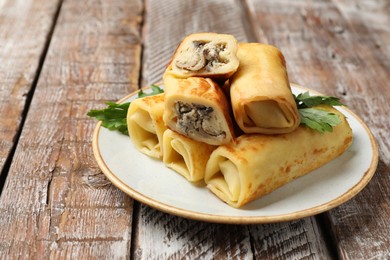 Photo of Delicious rolled crepes with mushrooms and parsley on wooden table, closeup