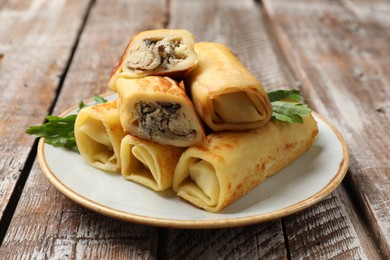 Photo of Delicious rolled crepes with mushrooms and parsley on wooden table, closeup